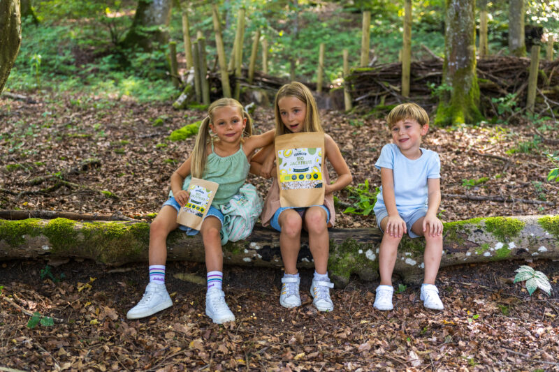 3 Kinder mit gefriergetrockneten Jackfruit auf einem Baumstamm
