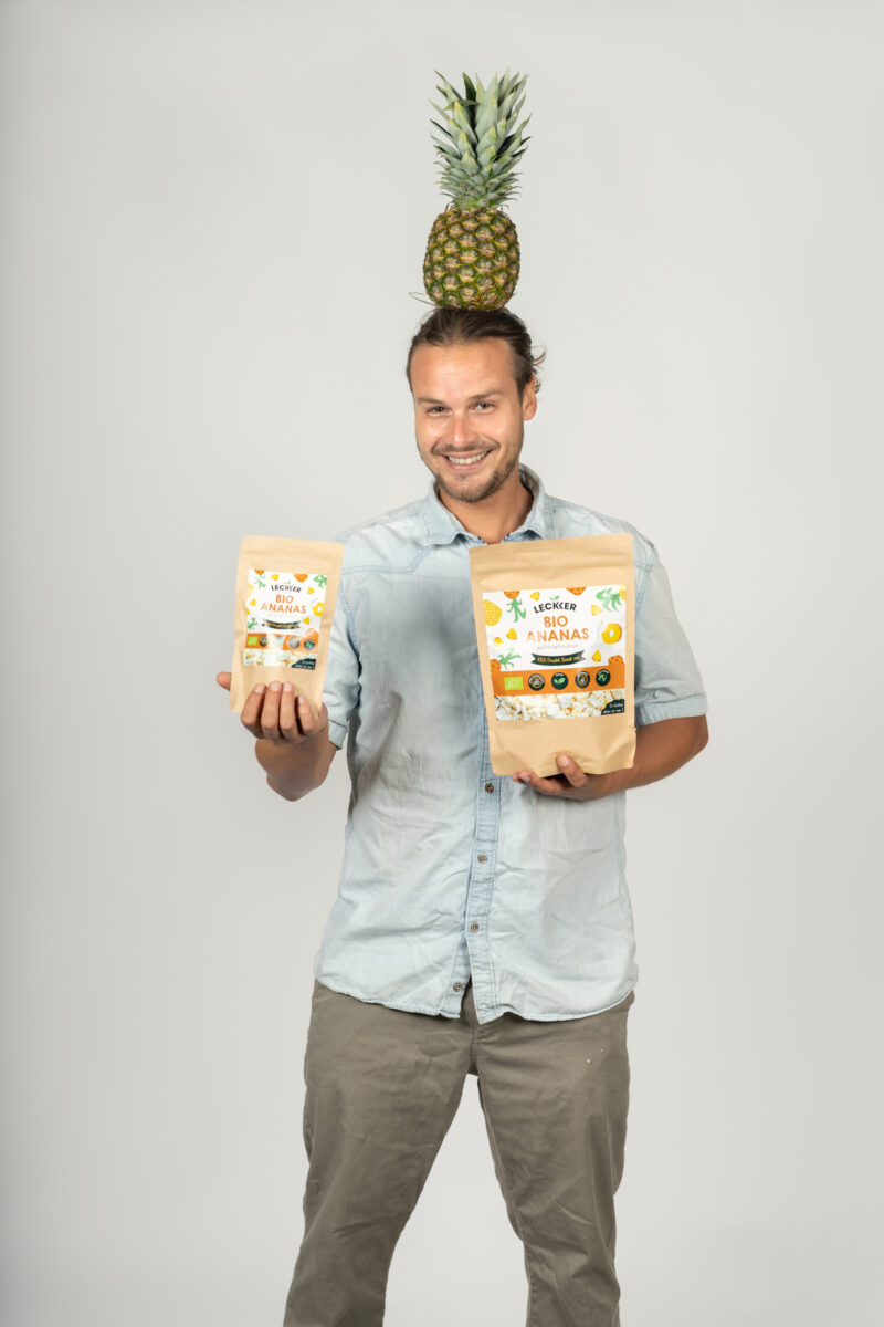 Mann mit gefriergetrockneter Ananas in den Händen und Ananas auf dem Kopf